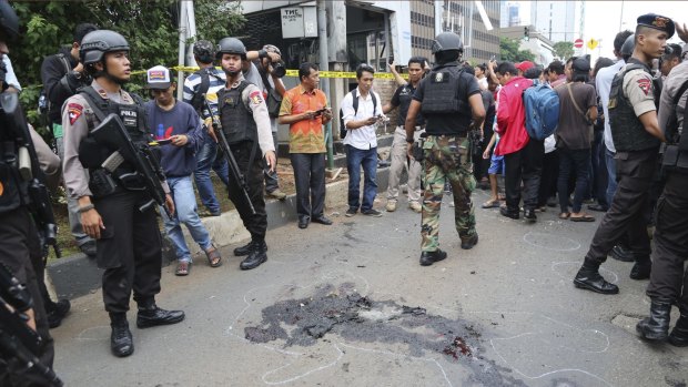 Police officers push back curious onlookers from the spot near a police post where an explosion went off in Jakarta.