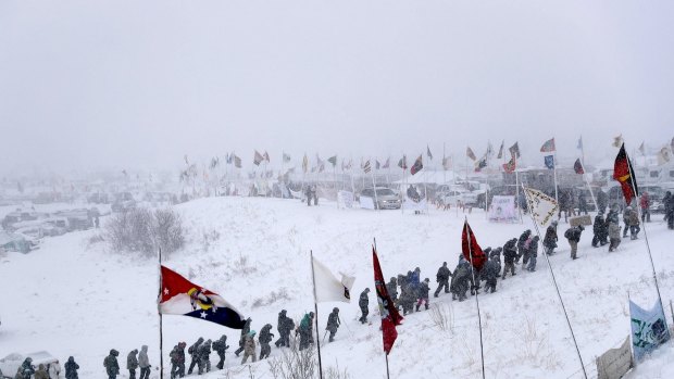 People walk out of the Oceti Sakowin camp as a march of military veterans and Native American tribal elders proceeds to a closed bridge across from the Dakota Access oil pipeline site in Cannon Ball, N.D., Monday, Dec. 5, 2016. (AP Photo/David Goldman)