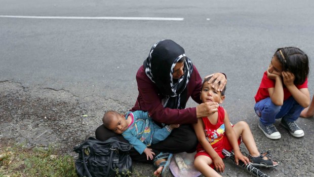 An Afghan migrant cleans a child's face as they rest on the side of a road after crossing the border from Serbia.