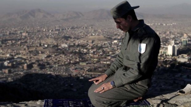 Uncertain future: An Afghan police officer prays on a mountain overlooking on Thursday. 