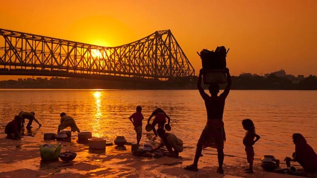 Water world: Families wash by a vast bridge over the Hooghly River, Kolkata.