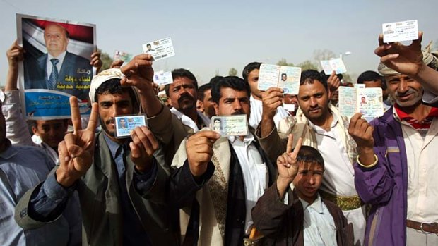 Yemeni men show their identity cards as they line up outside a polling station to cast their votes.