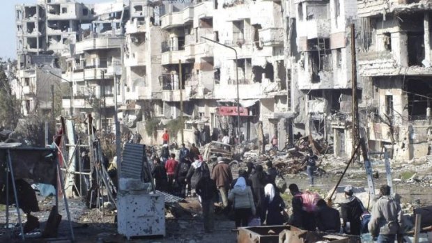Civilians carry their belongings as they walk towards a meeting point to be evacuated from a besieged area of Homs