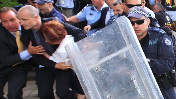 Prime Minister Julia Gillard is shielded from protesters as she leaves a Canberra restaurant yesterday.