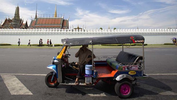 A driver waits for customers near the wall of the Grand Palace.