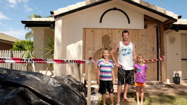 Robert Barlow and his daughters Caitlin,9 (left), and Sarah,6 (right), stand in front of a newly made wooden wall after a car crashed through their house in the early hours of the morning in Coolnwynpin Way in Capalaba, Feb. 9, 2013.