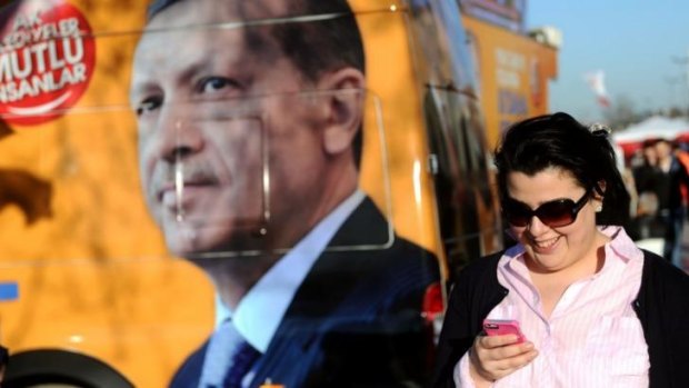 A Turkish woman checks her smartphone as she walks past a portrait of Turkish Prime Minister Recep Tayyip Erdogan.