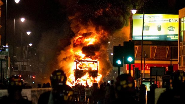 A double decker bus burns as riot police try to contain a large group of people on a main road in Tottenham, north London on Saturday.