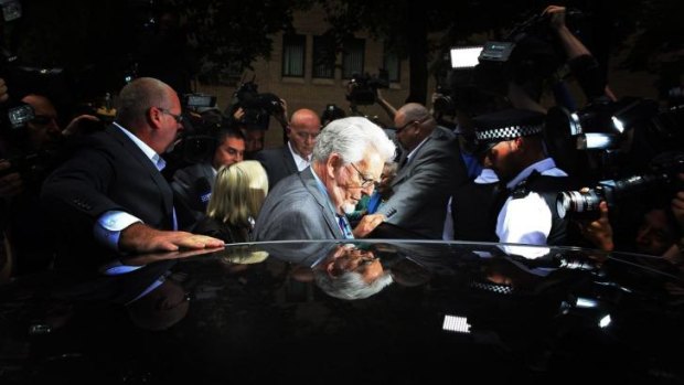 Rolf Harris is surrounded by the media during his trial in London.