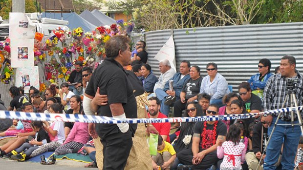 Fire survivor Tau Tafua, with bandages on his burnt arms, with his daughter Treicee outside the home this afternoon, with a crowd of mourners waiting for the final two bodies to be removed.
