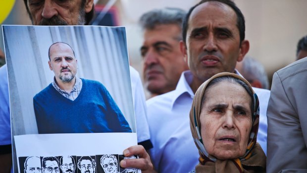 Flanked by a photograph of <i>Cumhuriyet</i> newspaper's investigative journalist Ahmet Sik, top left, and images of other defendants, left, Emine Yilmaz, 79, gathers outside a court in Istanbul.