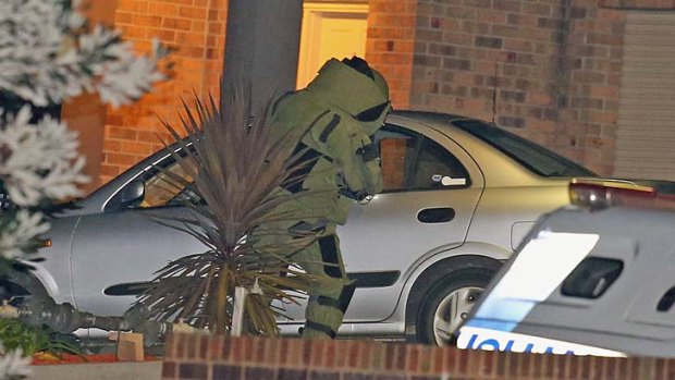 A police officer in a bomb suit inspects the car at the scene.