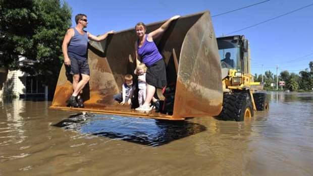 Patrick O'Toole, his wife Theresa and children Hayden, 6, and Hannah, 2, are driven to safety in a front-end loader after the Loddon River flooded their house at Bridgewater yesterday.