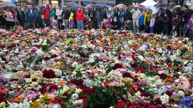 Floral tributes and candles cover the ground as friends and loved ones gather in the pouring rain outside Oslo cathedral .