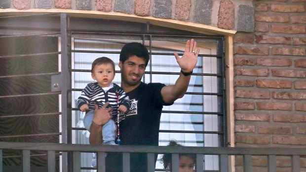 Resting his feet (and teeth) ... Uruguay's striker Luis Suarez, banned from football for four months after biting an opponent at the World Cup, holds his son Benjamin as he greets fans from his mother's home near Montevideo.
