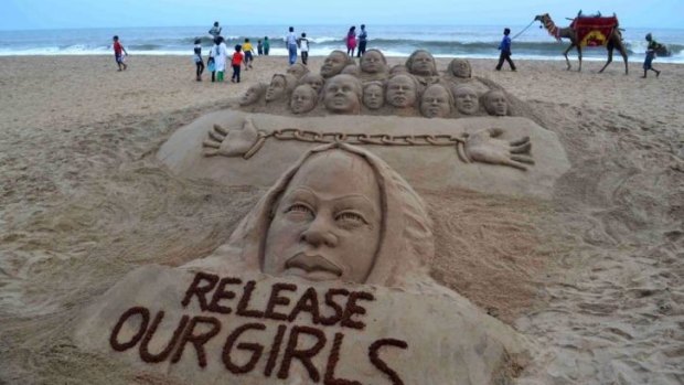Indian beachgoers pass a sand sculpture calling for the release of kidnapped school girls in Nigeria.