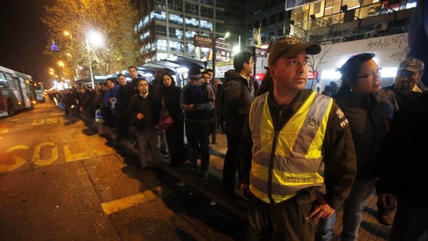 A police officer stands in the street to direct traffic as people stand in a line for public transportation after the earthquake.