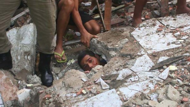 Carlos Eduardo Silva dos Santos, 24, peers out from under a wall where he is trapped as rescue workers try to free him after heavy rains in the Guarabita neighbourhood of Rio de Janeiro.