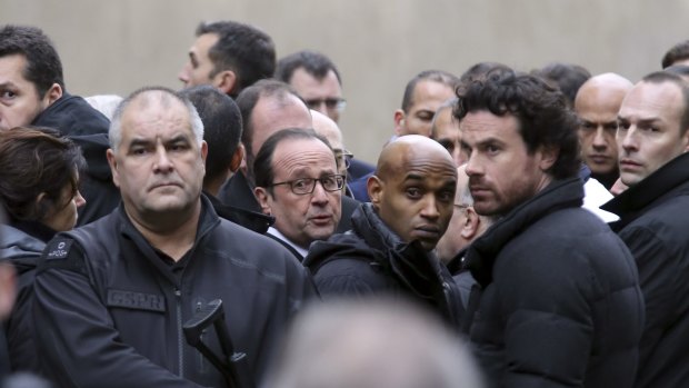 French President Francois Hollande, centre, flanked with security forces arrives outside the Charlie Hebdo office.