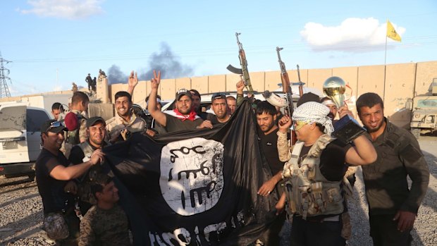 Iraqi security forces and allied Shiite militiamen celebrate as they hold a flag of the Islamic State group they captured in Tikrit.