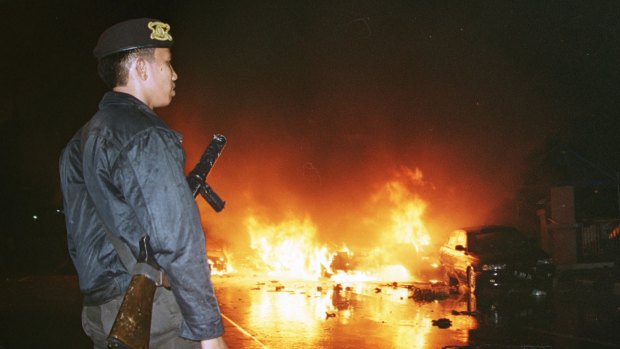 An Indonesian policeman watches as cars burn in the street following a bomb explosion in front of a church in Jakarta on December 24, 2000.