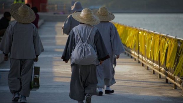 Monks walk past a railing lined with yellow ribbons with messages for the missing passengers.