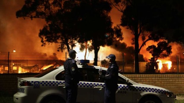 Police look on as several buildings burn during the Villawood riots in 2011.
