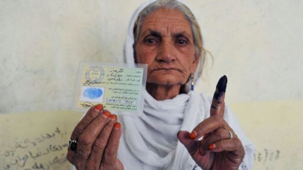 An Afghan woman holds up her inked finger and voter registration card after casting her ballot.
