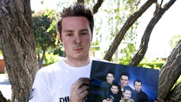 In shock...Tim de Voight's brother Nathan holds a family portrait of Tim, back left, with his brothers and sister.