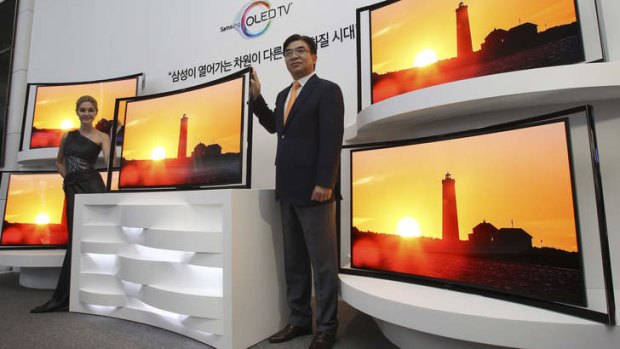 Kim Hyunsuk, the executive vice president of Samsung's TV division, right, poses with its 55-inch curved OLED TV during a press conference.