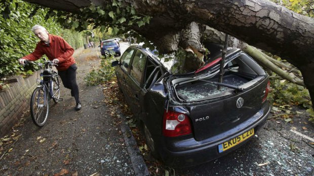 The damage: A car is crushed under a fallen tree as a man pushes a bicycle nearby following a storm, in Hornsey, north London.