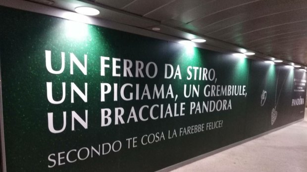 A Pandora advertisement targeting Christmas shoppers in Italy. The text says 'An iron, pyjamas, an apron, a Pandora bracelet. What do you think would make her happy?'. December 2017.?