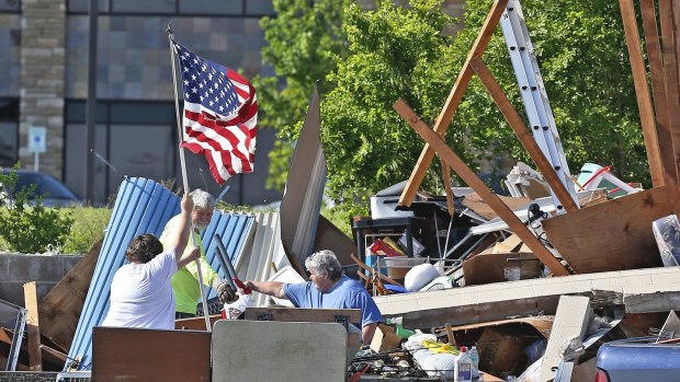 Jim Bresee, centre, smiles as his daughter, Sandra Silvy, left, raises a flag in what is left of the Bresee's storage unit following Wednesday's storm in Oklahoma City.