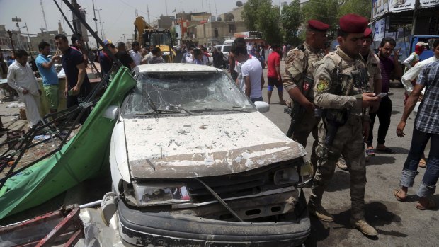 Security forces and citizens inspect the scene after a car bomb explosion at a crowded outdoor market in Sadr City.