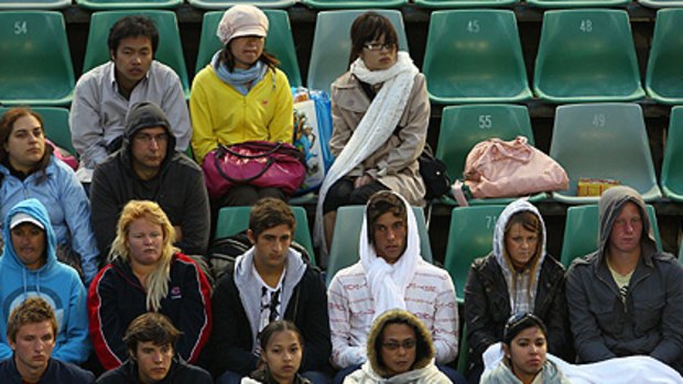 Spectators in the stands try to protect themselves from the rain and cold during the first round match between Bernard Tomic and Guillaume Rufin.
