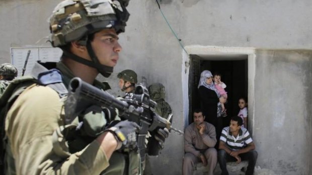 Palestinians sit outside their house as Israeli soldiers patrol near the West Bank City of Hebron.