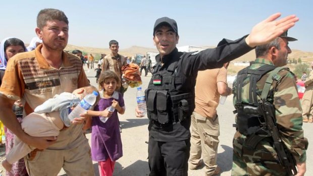 Peshmerga forces hand out water bottles and show the way to displaced Iraqi families from the Yazidi community as they cross the Iraqi-Syrian border at the Fishkhabur crossing, in northern Iraq. Thousands are fleeing  the siege of Mount Sinjar by Islamic State militants.
