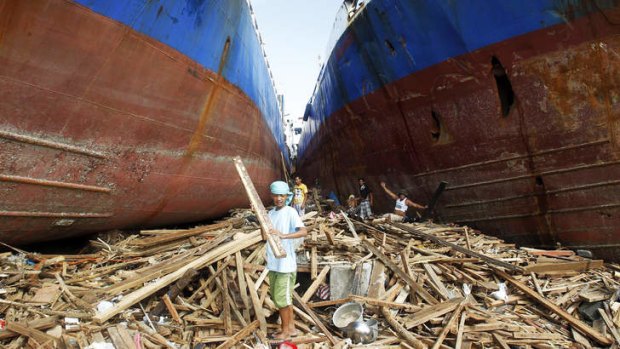 Residents pick up wood between two cargo ships washed ashore after super typhoon Haiyan hit.