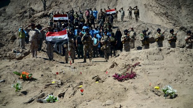 Iraqi soldiers salute this week as they stand next to a mass grave for Shi'ite soldiers from Camp Speicher.