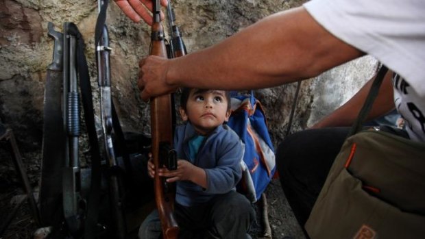 A child tries to help his father arrange weapons at a checkpoint set up by the Self-Defence Council of Michoacan in Tancitaro, Mexico.