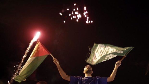 A Palestinian man waves a national and a Hamas flag under fireworks.