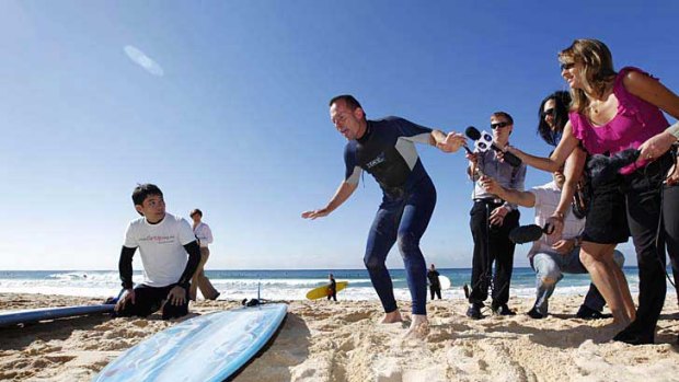 Reporters listen in as Opposition Leader Tony Abbott gives former refugee Riz Wakil some surfing tips on Manly beach.