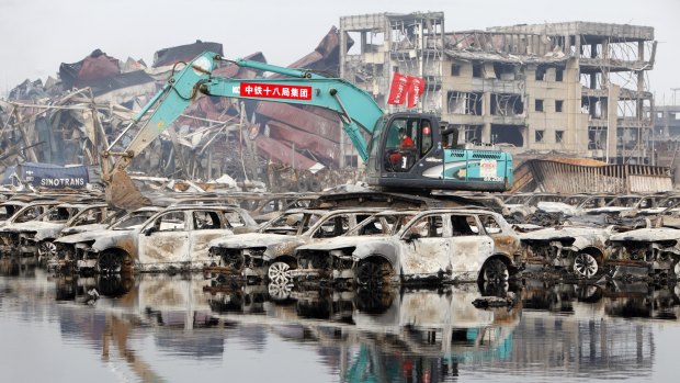 Rescuers and machines clean up burnt vehicles at the blast site.