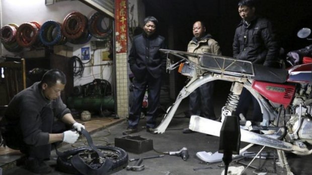 Lu Qiao and his  brothers watch as a roadside mechanic replaces a tyre on their motorcycle.