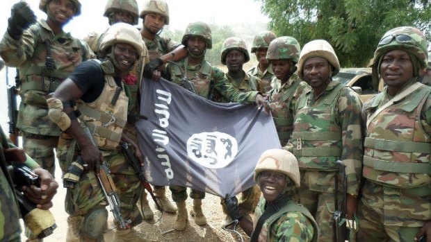 Nigerian troops pose with a flag of Boko Haram after dismantling terrorists from their camp along Djimitillo Damaturu Road, Yobe State in northeastern Nigeria, following fierce fighting there.