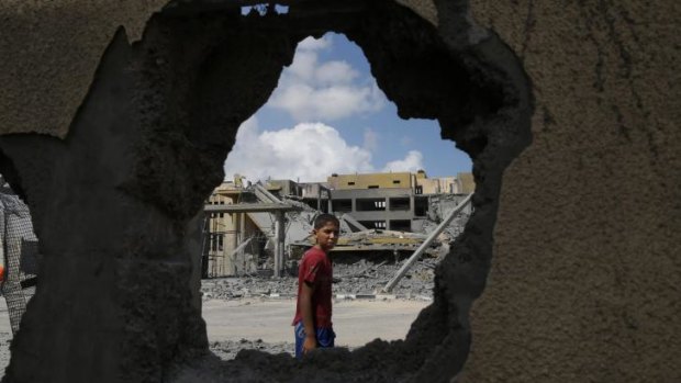 A Palestinian boy walks past damaged buildings after an Israeli airstrike.