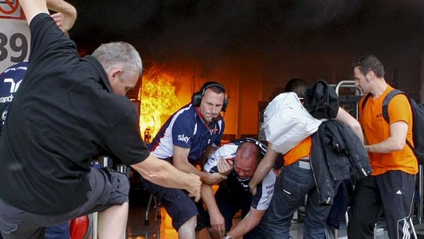 Williams team mechanics help a colleague after the fire erupted.
