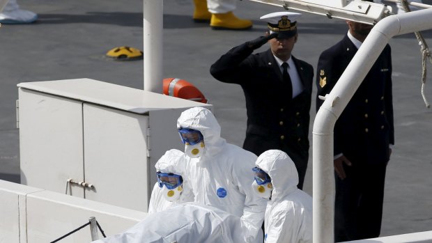 An Italian coastguard officer salutes as rescuers carry the body of one of Sunday's victims off a ship in Valletta's Grand Harbour.