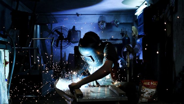 A worker wearing a protective mask cuts a sheet of steel.