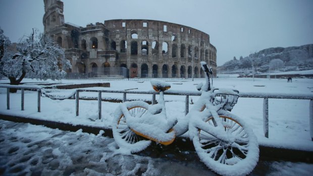 A bicycle is parked in front the ancient Colosseum during a snowfall in Rome.